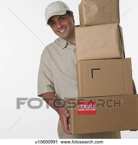 Stock Image - Studio shot of deliveryman holding stack of boxes. Fotosearch