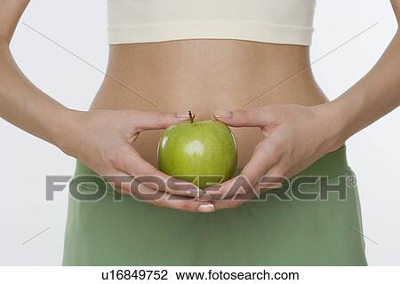 Studio shot of woman holding apple in front of belly View Large Photo Image Stock Image - Studio shot of woman holding apple in front of belly. Fotosearch