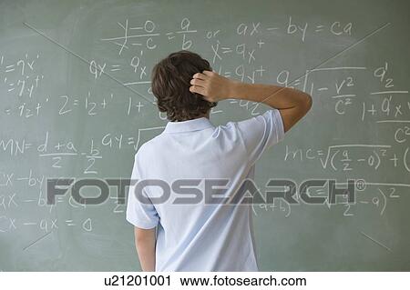 Stock Image - Teenaged boy looking at math equations on blackboard. Fotosearch