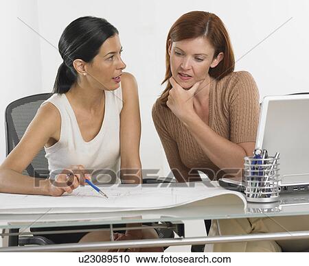 Stock Image - Two businesswomen looking at blueprints. Fotosearch