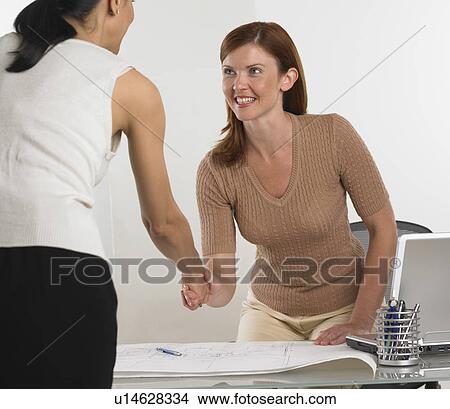Two businesswomen shaking hands over blueprints View Large Photo Image Picture - Two businesswomen shaking hands over blueprints. Fotosearch