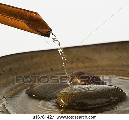 Stock Photo - Water pouring out of plant stalk into bowl with stones. Fotosearch