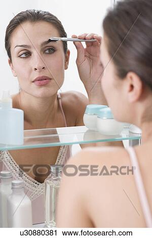 Stock Image - Woman combing eyebrows in mirror. Fotosearch