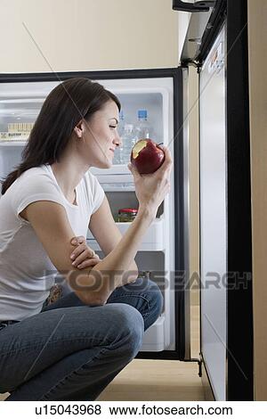 Woman eating apple in front of open refrigerator View Large Photo Image Stock Photo - Woman eating apple in front of open refrigerator. Fotosearch