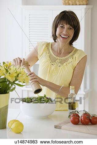 Stock Image - Woman grinding pepper onto salad. Fotosearch