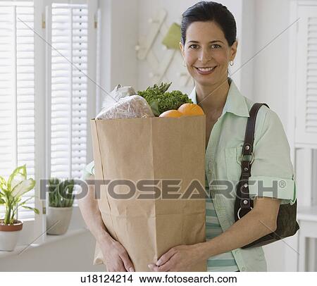 Picture - Woman holding bag of groceries in kitchen. Fotosearch