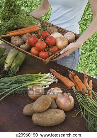 Stock Image - Woman holding basket of fresh vegetables. Fotosearch