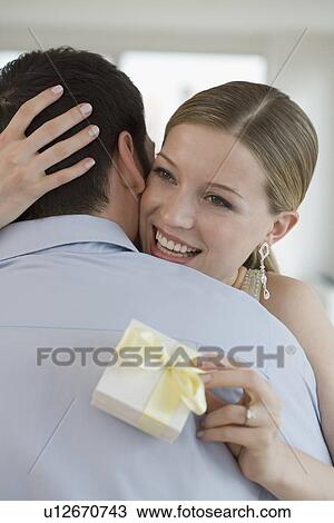Stock Image - Woman holding gift and hugging husband. Fotosearch