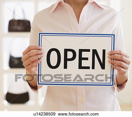 Stock Photo - Woman holding Open sign in boutique. Fotosearch