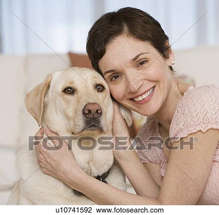 Stock Image - Woman hugging dog in livingroom. Fotosearch