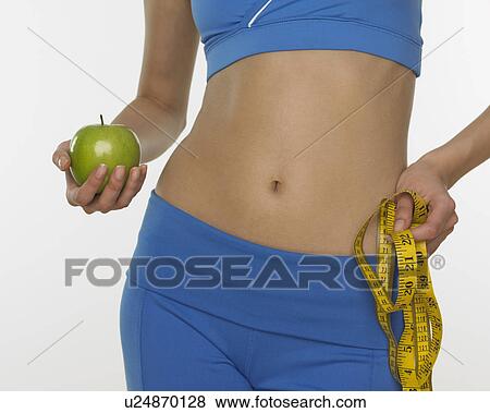 Woman in athletic gear holding apple and tape measure View Large Photo Image Stock Photo - Woman in athletic gear holding apple and tape measure. Fotosearch