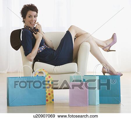 Stock Photo - Woman in chair next to shopping bags. Fotosearch
