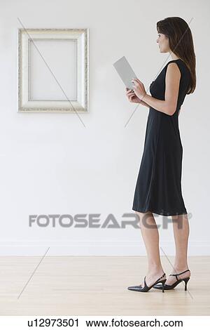 Stock Image - Woman in evening dress next to empty picture frame. Fotosearch