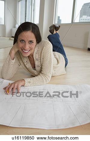 Stock Image - Woman laying on floor with blueprints. Fotosearch