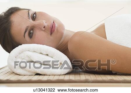 Stock Image - Woman laying on mat with rolled towel under neck. Fotosearch
