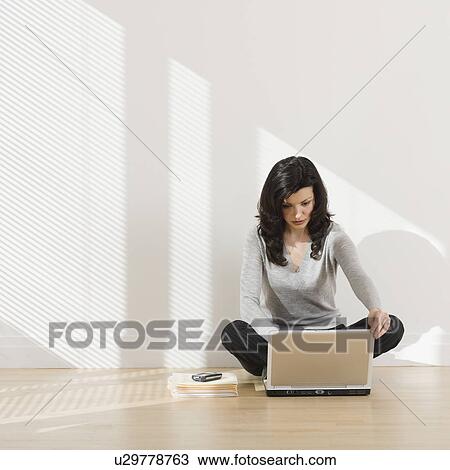 Stock Image - Woman looking at laptop on floor. Fotosearch