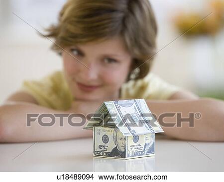 Picture - Woman looking at model house made of US dollars. Fotosearch