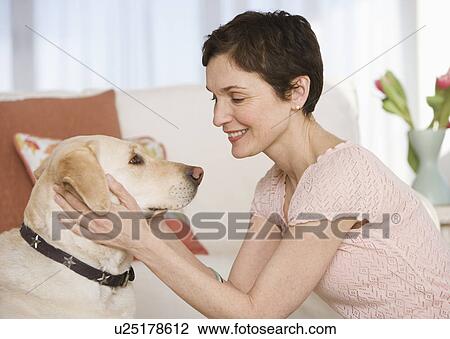 Woman petting dog in livingroom View Large Photo Image Stock Image - Woman petting dog in livingroom. Fotosearch