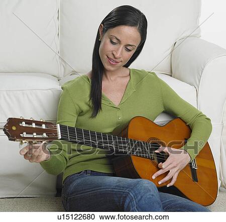 Stock Image - Woman playing guitar on sofa. Fotosearch