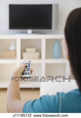 Stock Image - Woman pointing remote control at television. Fotosearch