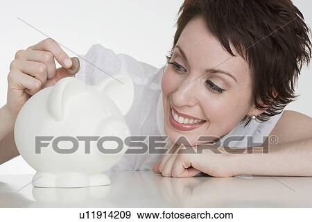 Woman putting coin in piggy bank View Large Photo Image Stock Photo - Woman putting coin in piggy bank. Fotosearch