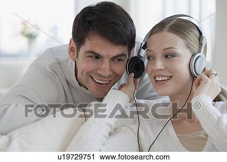 Stock Image - Woman sharing headphones with husband. Fotosearch
