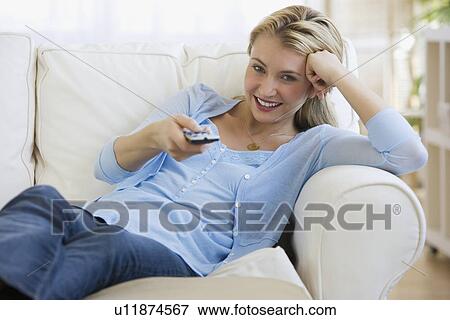 Woman sitting on sofa pointing remote control View Large Photo Image Stock Photo - Woman sitting on sofa pointing remote control. Fotosearch