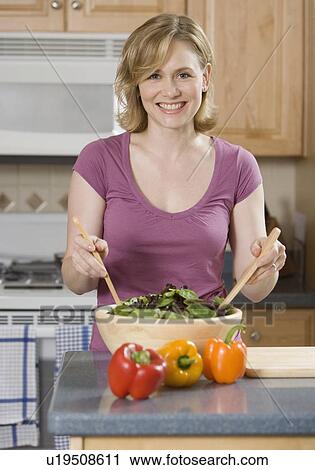 Stock Image - Woman tossing salad in kitchen. Fotosearch