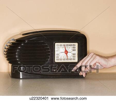 Stock Image - Woman turning knob on old fashioned radio. Fotosearch