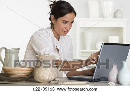 Stock Image - Woman using laptop next to pottery. Fotosearch