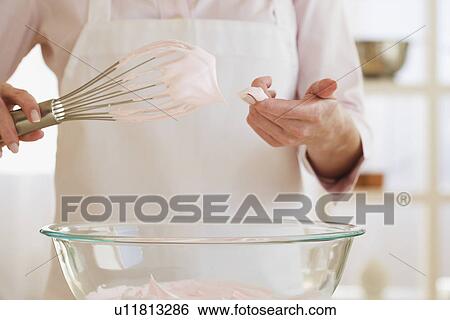 Stock Photograph - Woman wiping batter from whisk with finger. Fotosearch