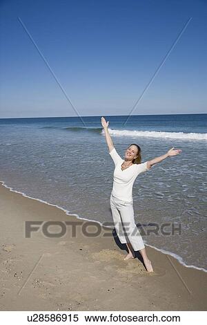 Stock Photography - Woman with arms raised at beach. Fotosearch