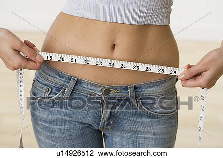 Stock Image - Woman with bare midriff measuring waist. Fotosearch