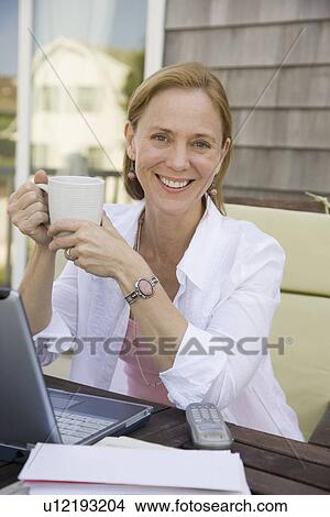 Picture - Woman with coffee mug next to laptop. Fotosearch