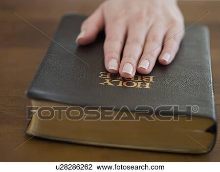 Stock Image - Woman's hand on Bible. Fotosearch