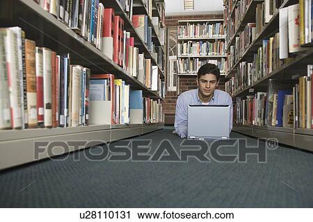 Stock Image - Young man with laptop in library. Fotosearch