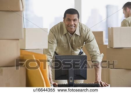 Stock Photography - African delivery man next to computer. Fotosearch