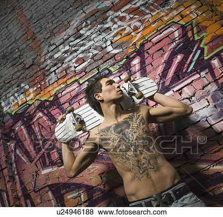 Asian man holding skate board in front of graffitied wall View Large Photo Image Stock Photo - Asian man holding skate board in front of graffitied wall. Fotosearch