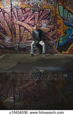Asian man sitting in front of graffitied wall View Large Photo Image Stock Photograph - Asian man sitting in front of graffitied wall. Fotosearch