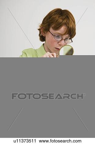 Stock Image - Boy examining item with magnifying glass. Fotosearch
