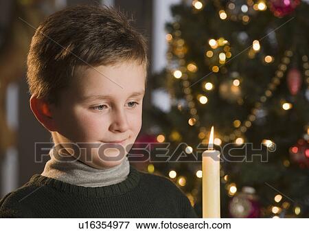 Stock Photo - Boy looking at candle in front of Christmas tree. Fotosearch