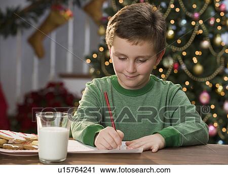 Stock Image - Boy writing letter in front of Christmas tree. Fotosearch