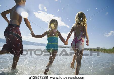 Stock Photo - Brother and sisters running in water, Utah, United States. Fotosearch