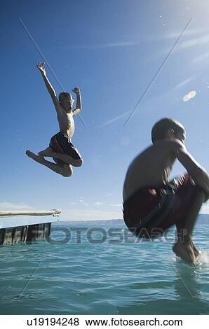 Stock Photo - Brothers jumping off dock into lake, Utah, United States. Fotosearch