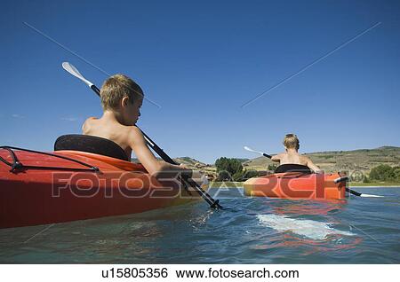 Stock Photograph - Brothers paddling in canoes on lake, Utah, United States. Fotosearch