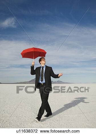 Stock Image - Businessman walking with umbrella, Salt Flats, Utah, United States. Fotosearch