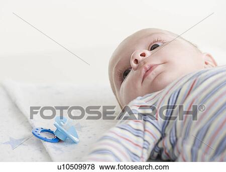 Stock Photo - Close up of baby lying down next to pacifier. Fotosearch