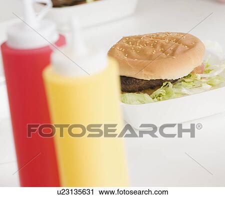 Stock Image - Close up of hamburger and condiment bottles. Fotosearch