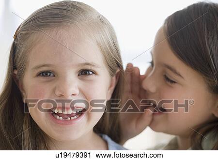 Stock Image - Close up of sisters telling secret. Fotosearch