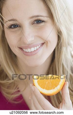 Stock Photograph - Close up of woman holding orange wedge. Fotosearch